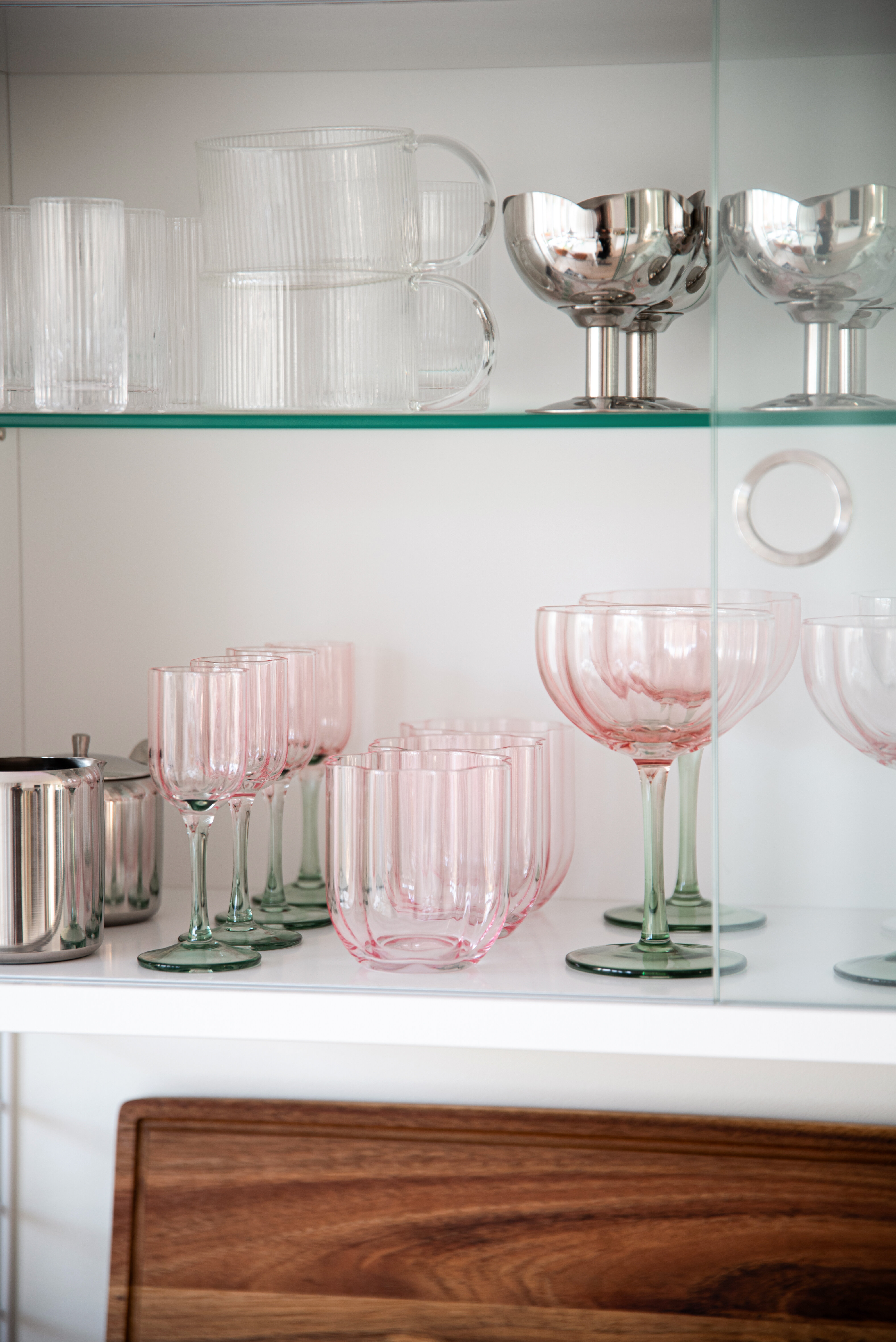 Pink and green drinking glasses displayed on glass shelves