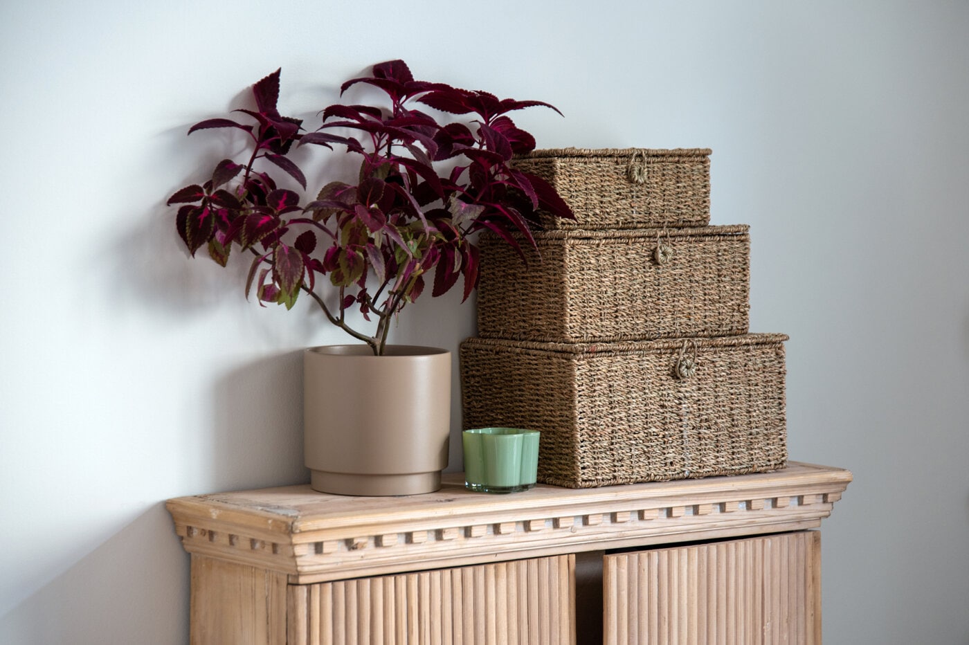 Woven storage baskets stacked beside a potted plant on a wooden cabinet.