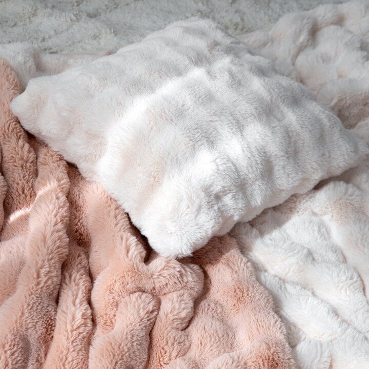 Soft faux fur cushion on a pink knitted blanket.