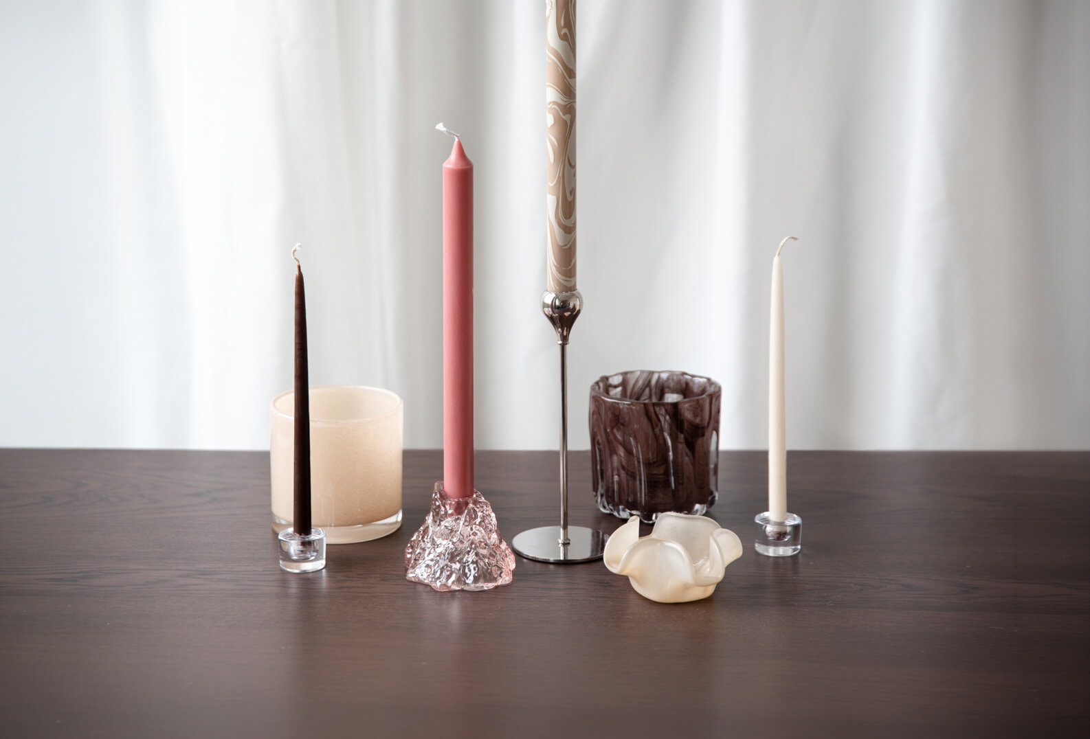A selection of candle holders, candles and glass lanterns displayed on a table.