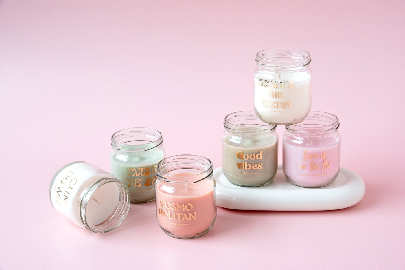 Scented candles in glass jars with text against pink bakground