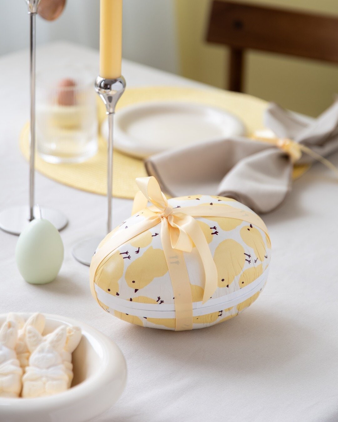 An Easter egg with a satin ribbon placed on a decorated Easter table.