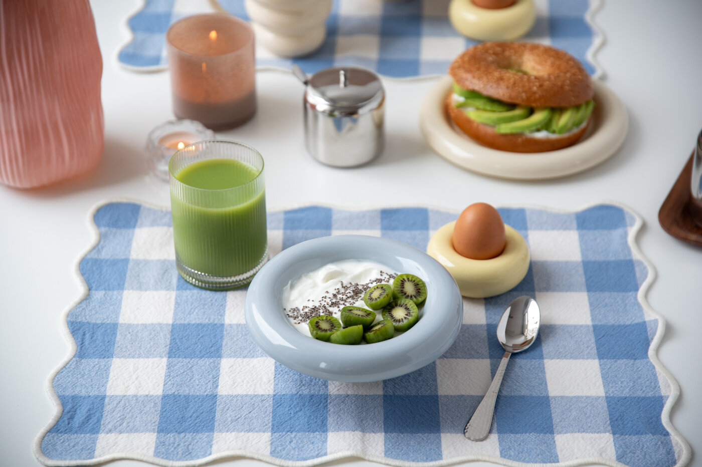 Breakfast table setting with a ribbed glass, light blue bowl and egg cup on a checkered placemat.