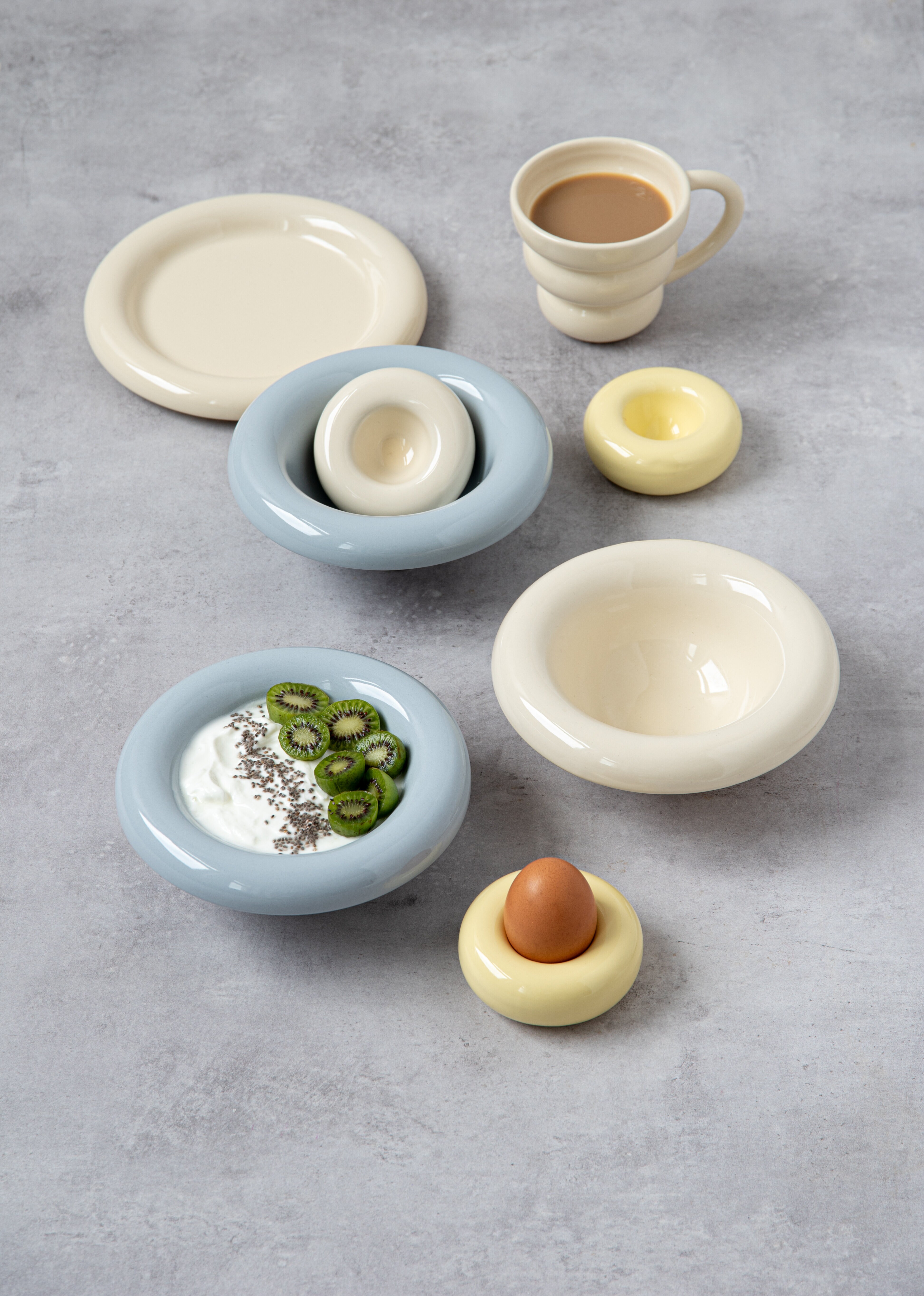 Bowls, egg cup and side plate with rounded shape in various colours on a light background.
