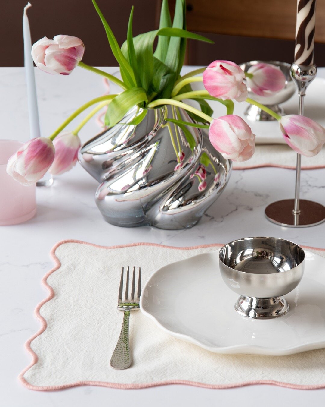 White placemat with pink edges and silver details in the table setting.