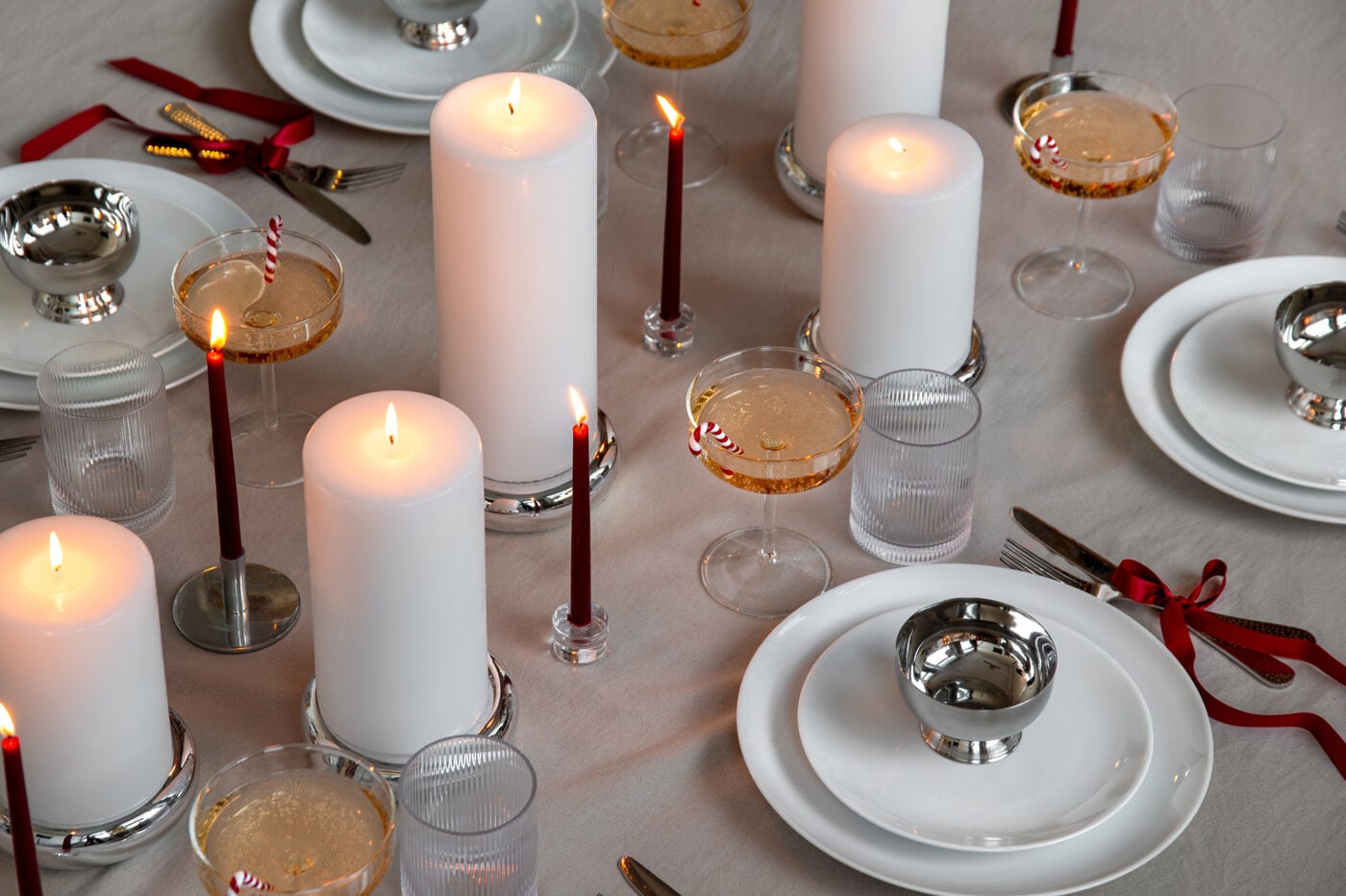 Festlig dukning med vita blockljus, smala röda ljus och champagneglas dekorerade med polkagriskäppar.