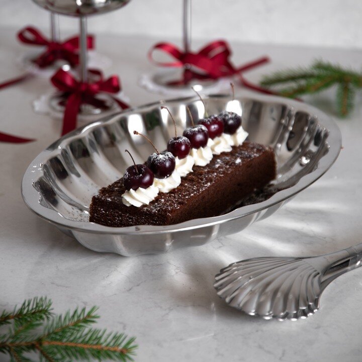 Chocolate cake with whipped cream and cherries served on a silver-coloured platter.