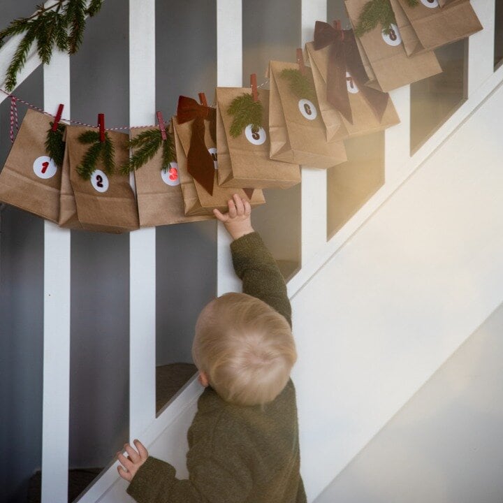 Child by a staircase with an Advent calendar made of small brown paper bags.