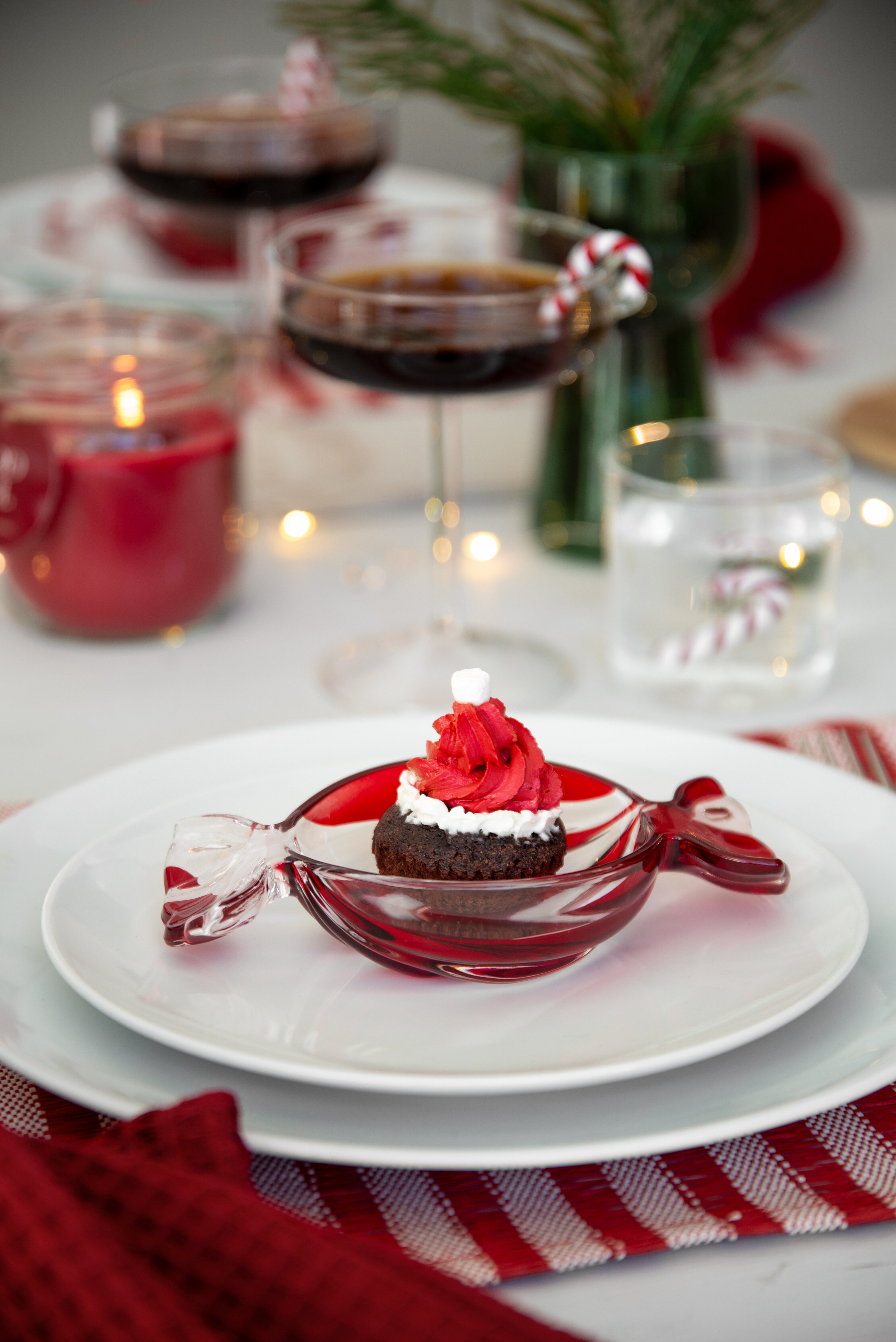 Christmas table setting with dessert in a glass bowl, red details and drinking glasses.