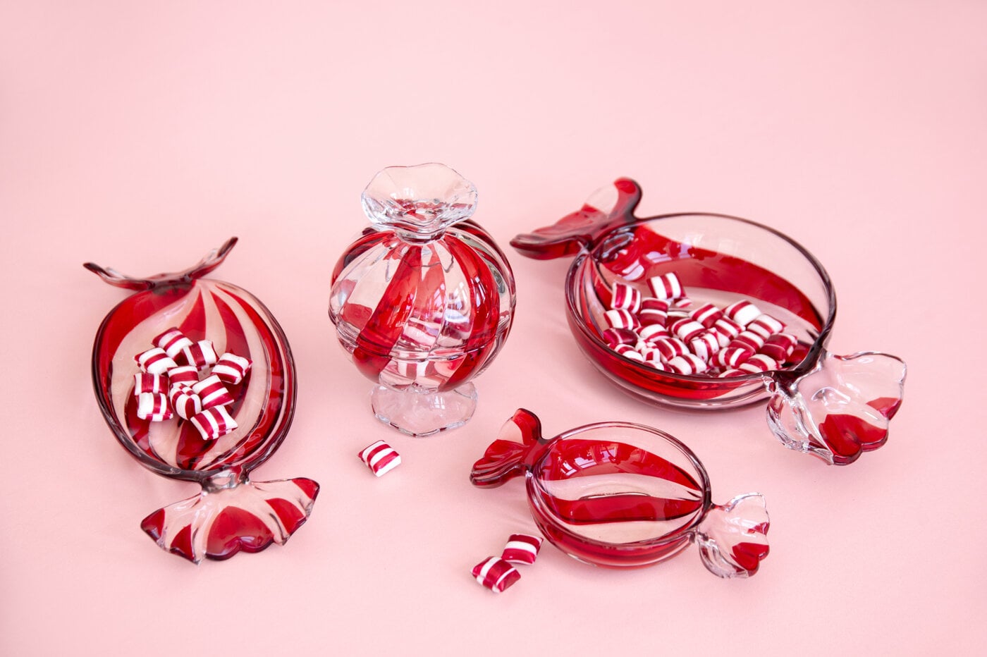 Red and clear glass bowls and a sweet jar with candy cane-inspired details against a pink background.