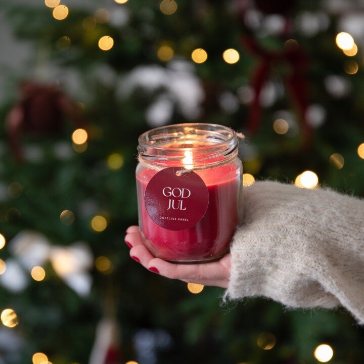 A red lit scented candle in front of a Christmas tree.
