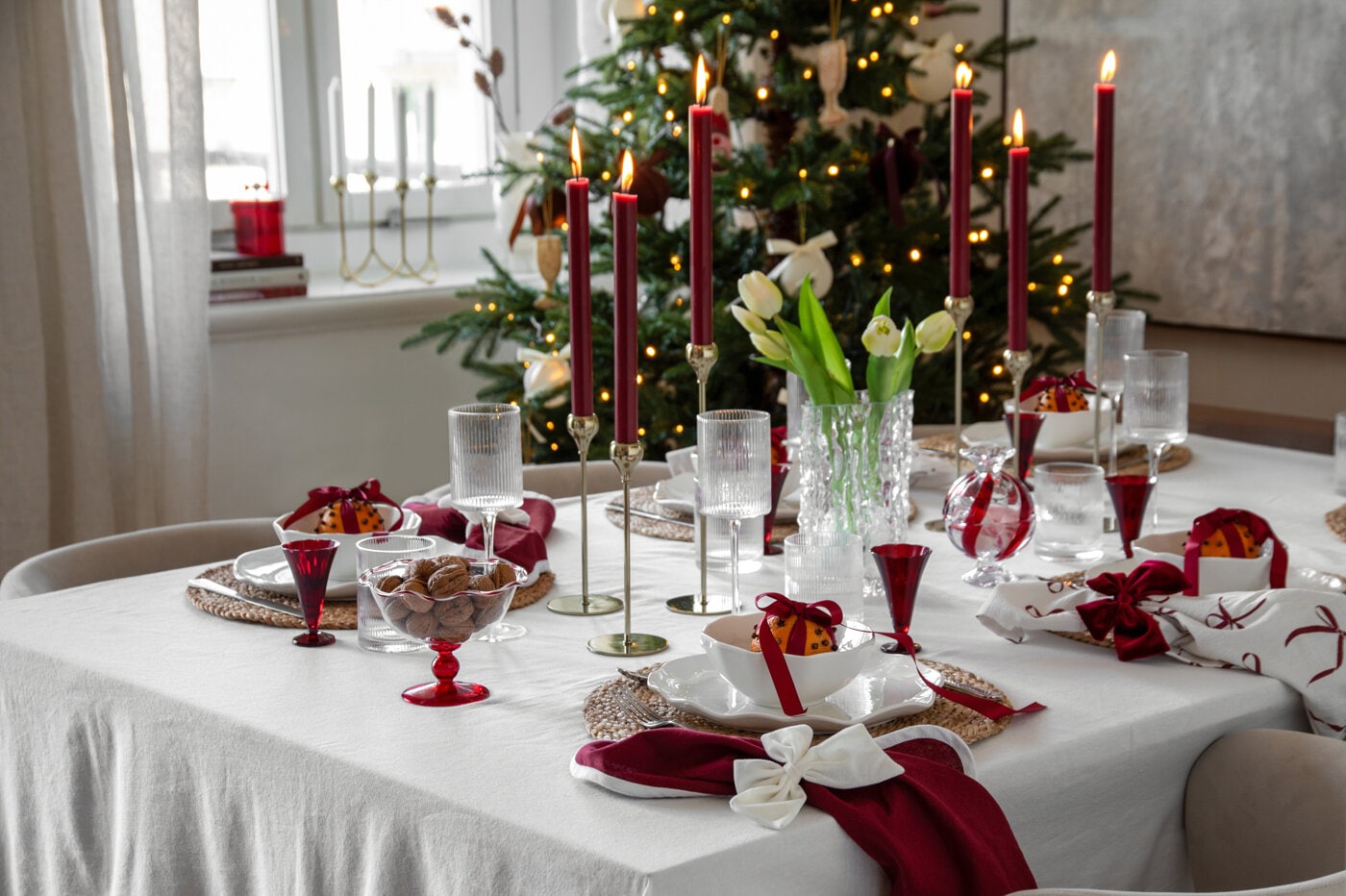 Christmas table setting in burgundy and white with lit candles, glassware and decorative bows.