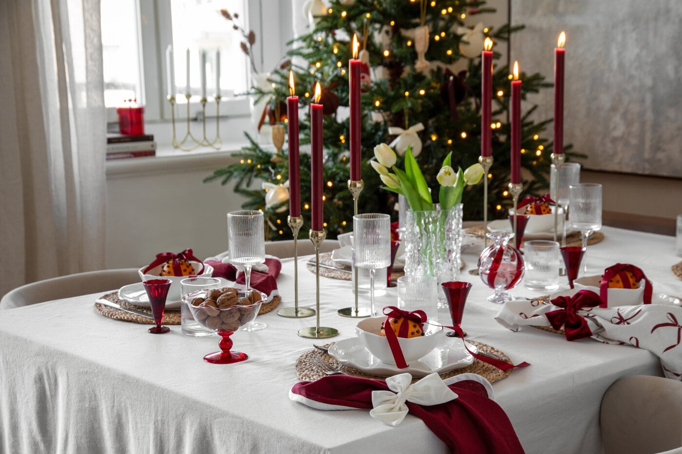 Christmas table setting in burgundy and white with lit candles, glassware and decorative bows.