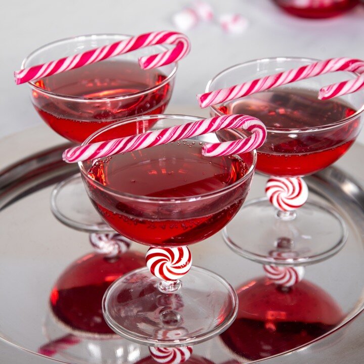 Cocktail glasses with a red drink and candy canes as decoration.