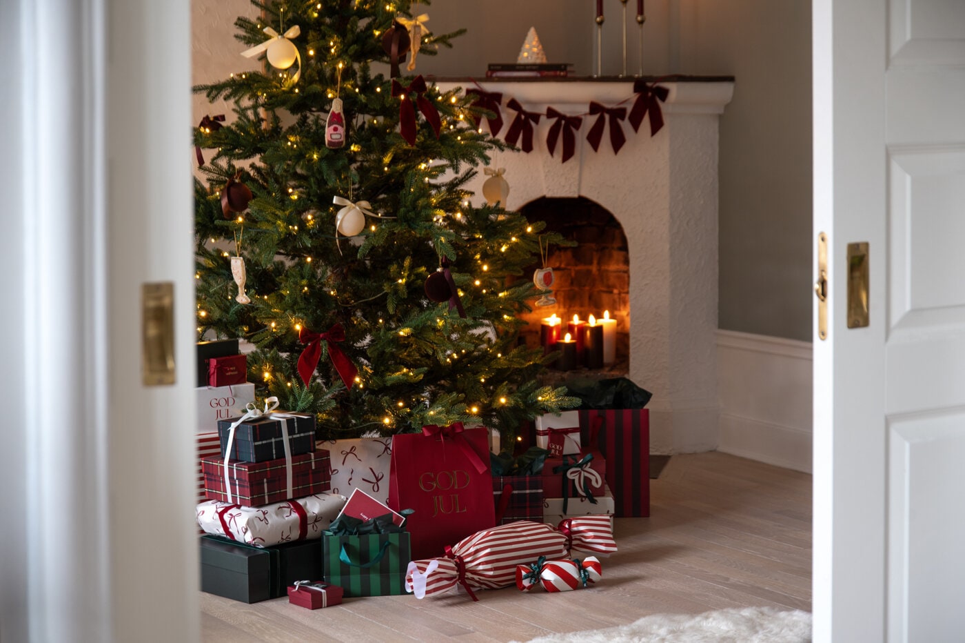 Decorated Christmas tree with lights and red bows, surrounded by wrapped gifts in front of a fireplace.