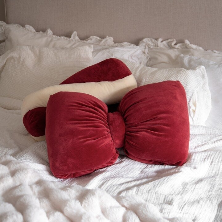 Red bow cushion and candy cane cushion on a white bed.