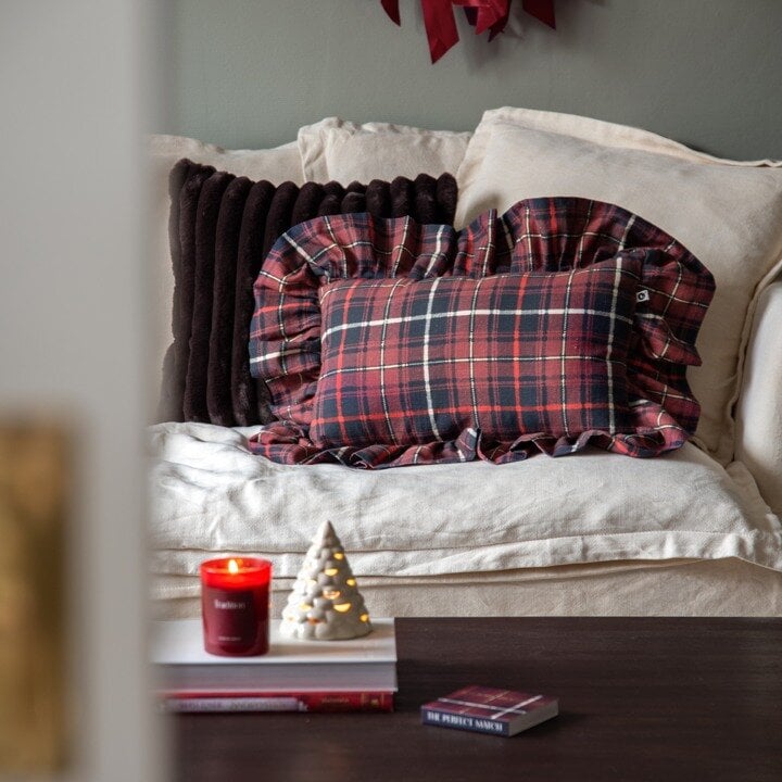 Christmas sofa setting with checked cushions, a lit candle and a decorative Christmas tree.