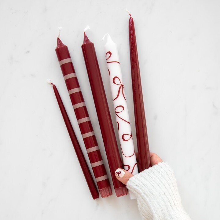 Burgundy and white taper candles with stripes and bow patterns.