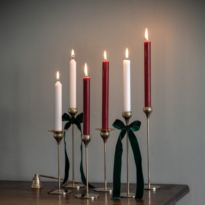 Red and white lit candles in tall candle holders with green bows.