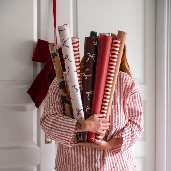 Person holding rolls of Christmas wrapping paper in red and white patterns.