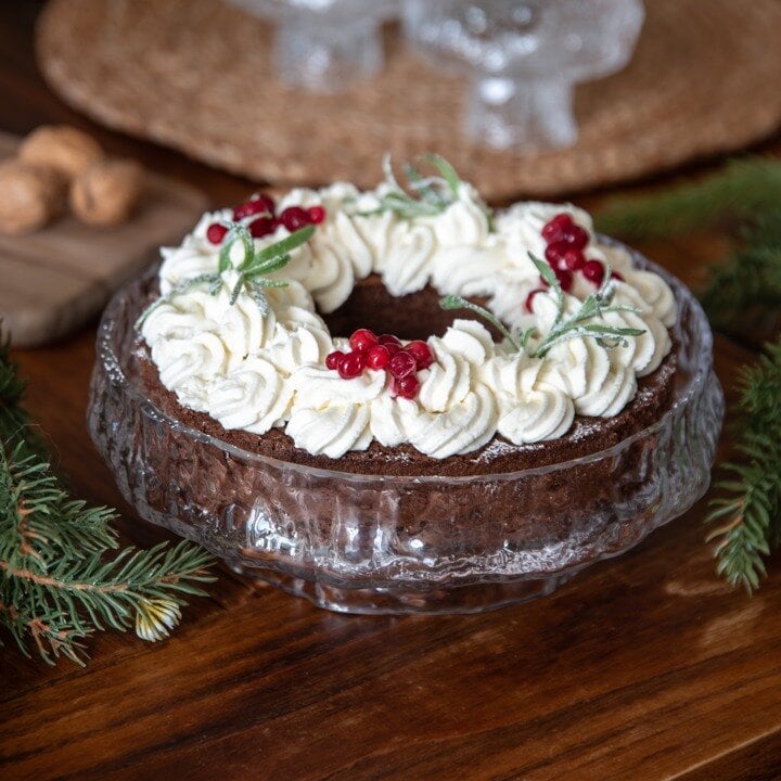 Christmas cake with white frosting and lingon berries on a set table.