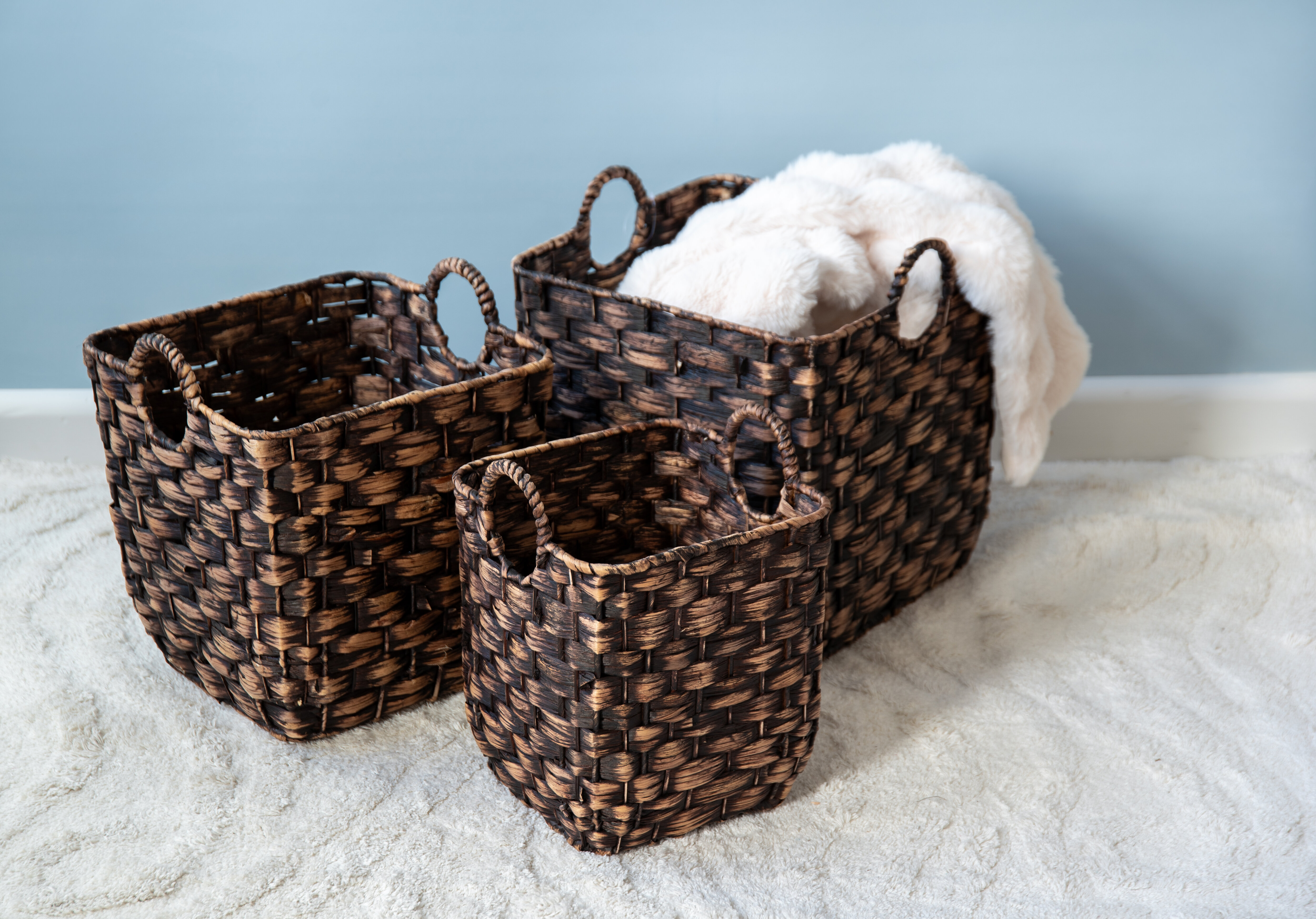 Woven storage baskets in different sizes with a soft white blanket draped over one basket.