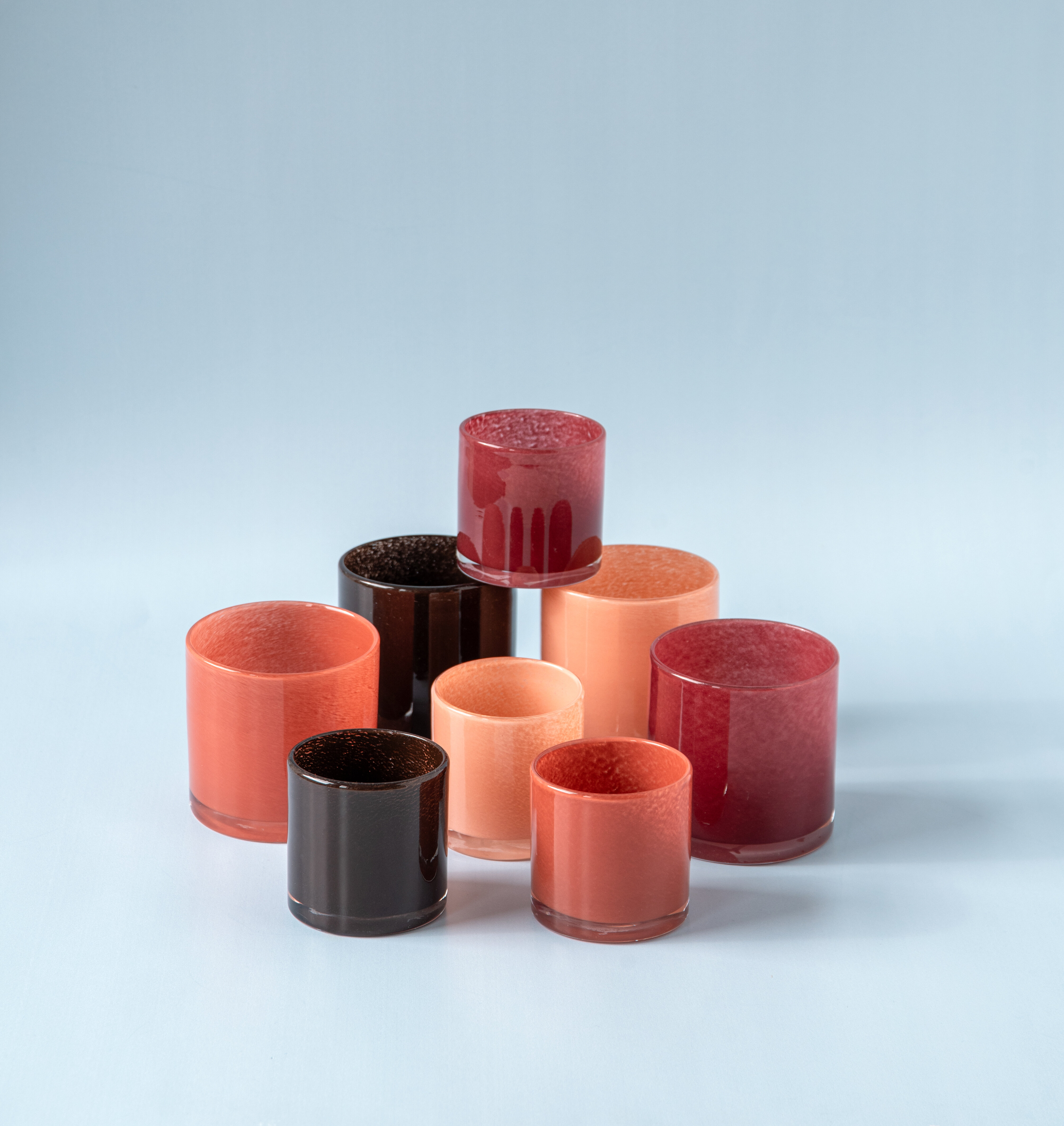 Group of colourful candle holders in brown and rusty tones against a light blue background.