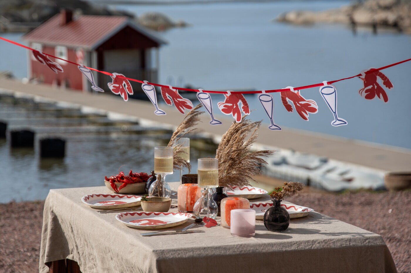 Outdoor crayfish party table set with a crayfish garland, plates, and candles by the waterfront.