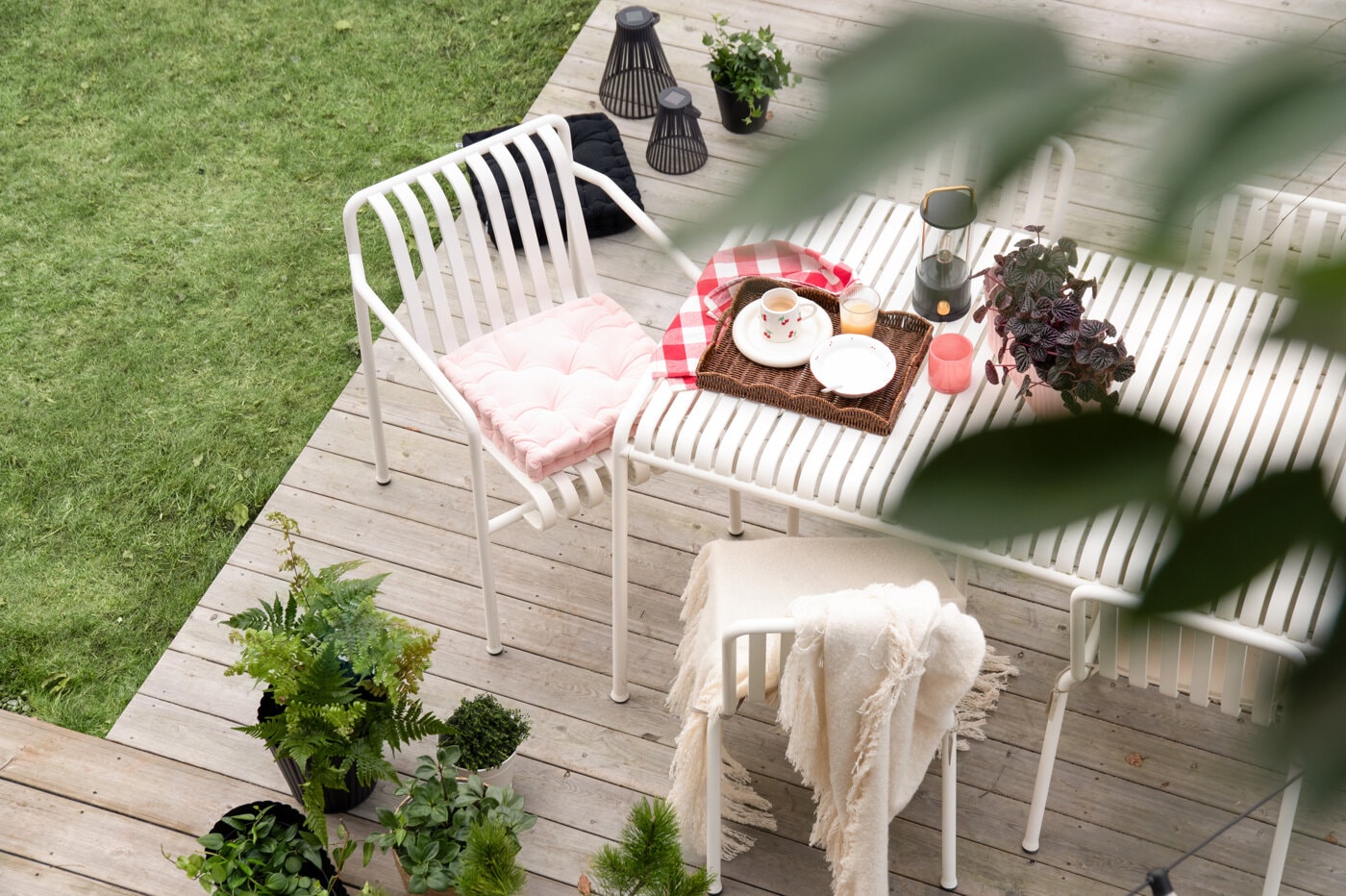 Patio with a white table and chair on a wooden deck, styled with a tray, coffee, and plants.