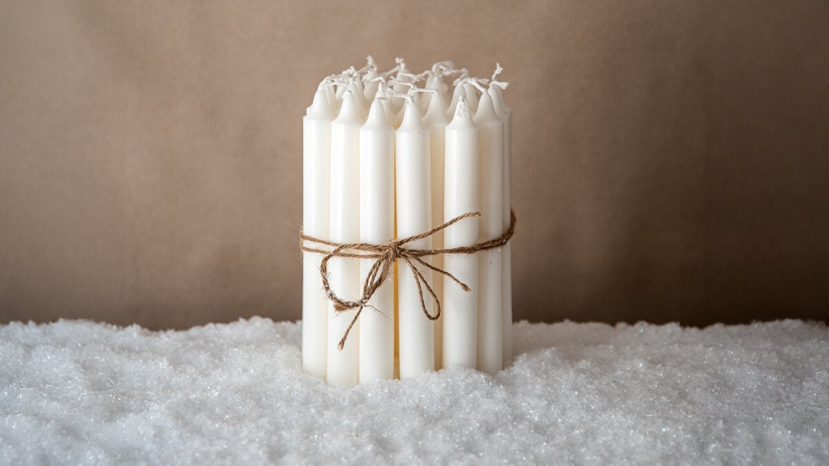 White candles tied together with string, placed on artificial snow.