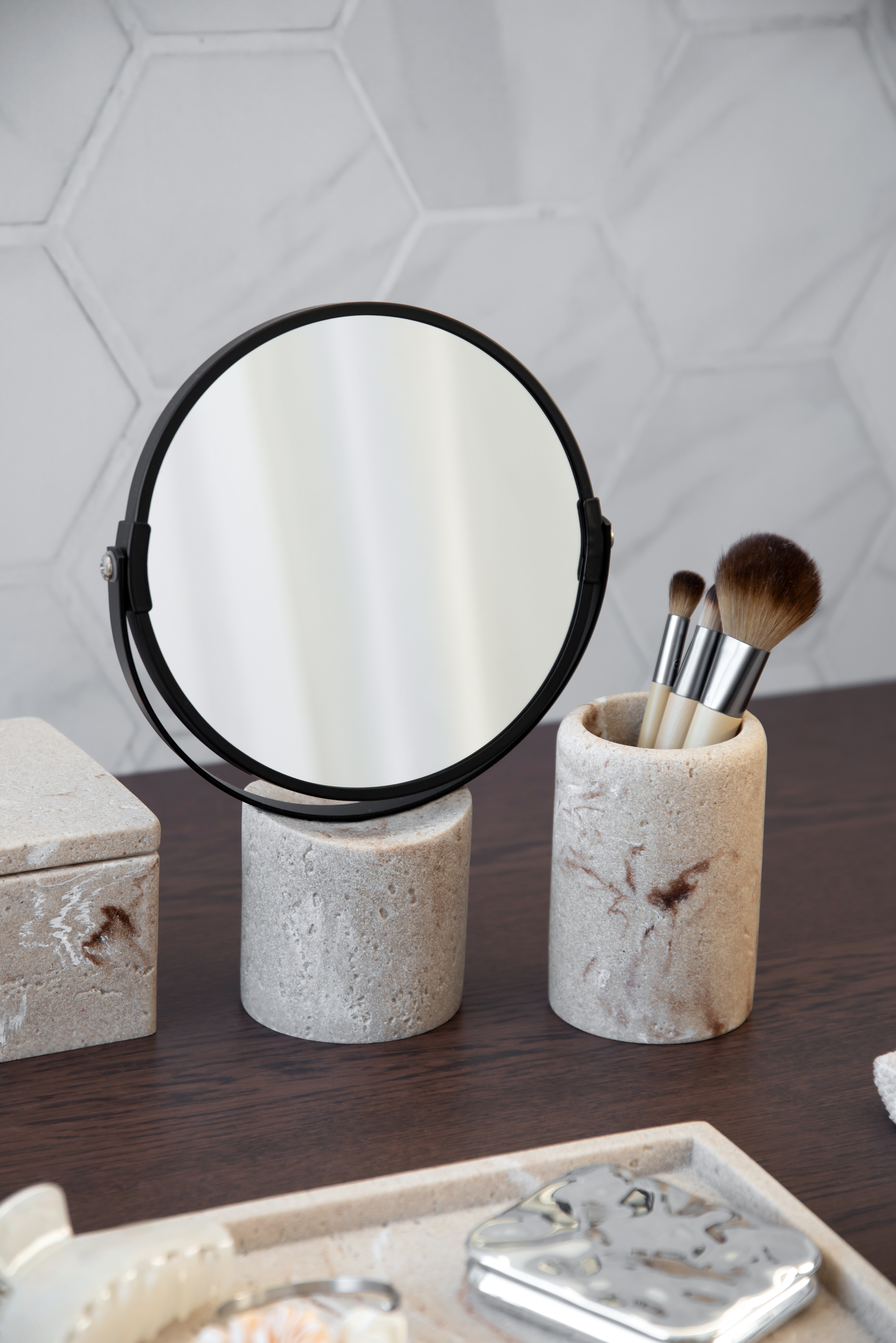 Round tabletop mirror with makeup brushes in decorative holders.