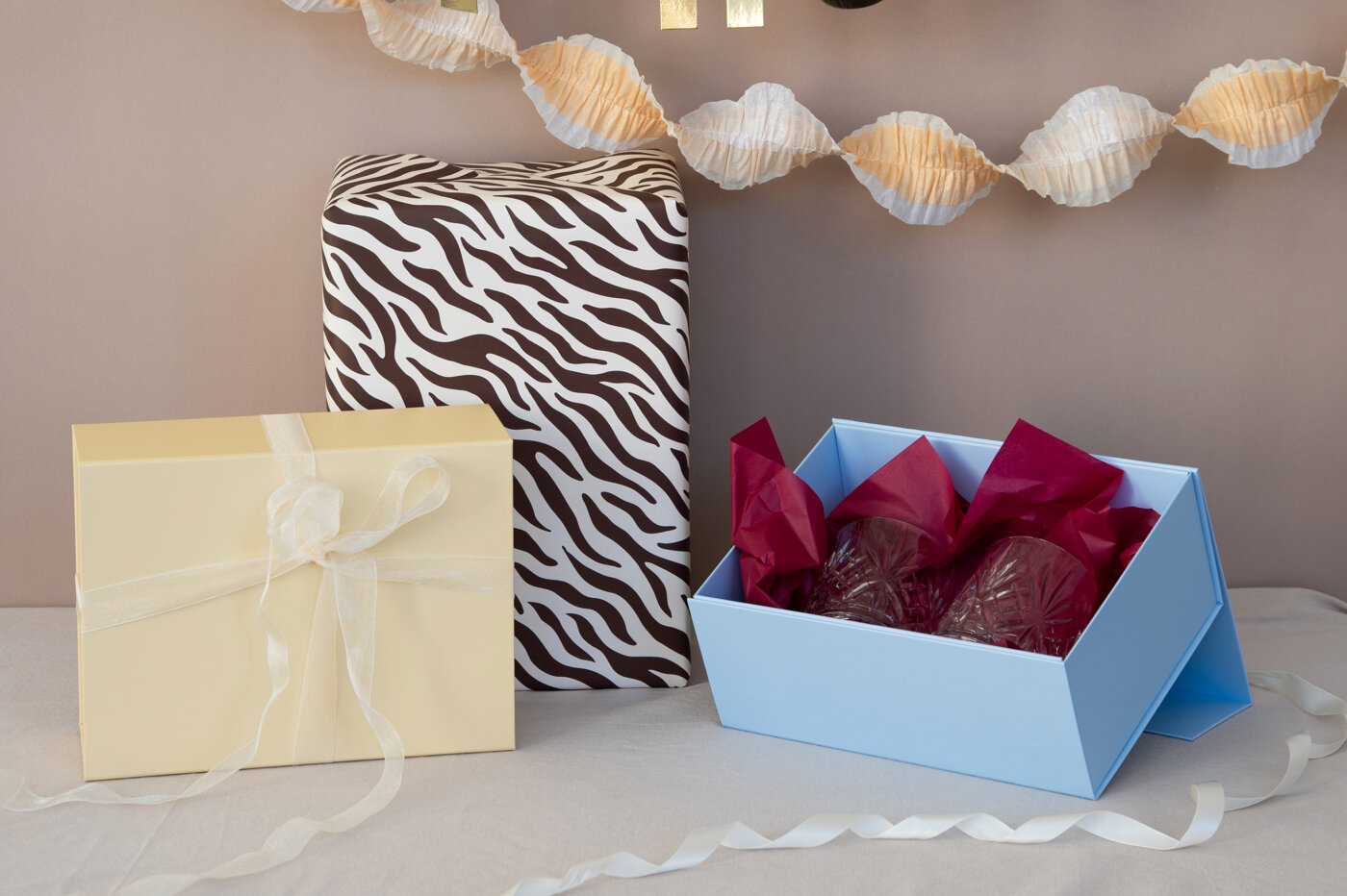 Gift wrapping with patterned gift, gift with satin ribbon, and open blue box with tissue paper.