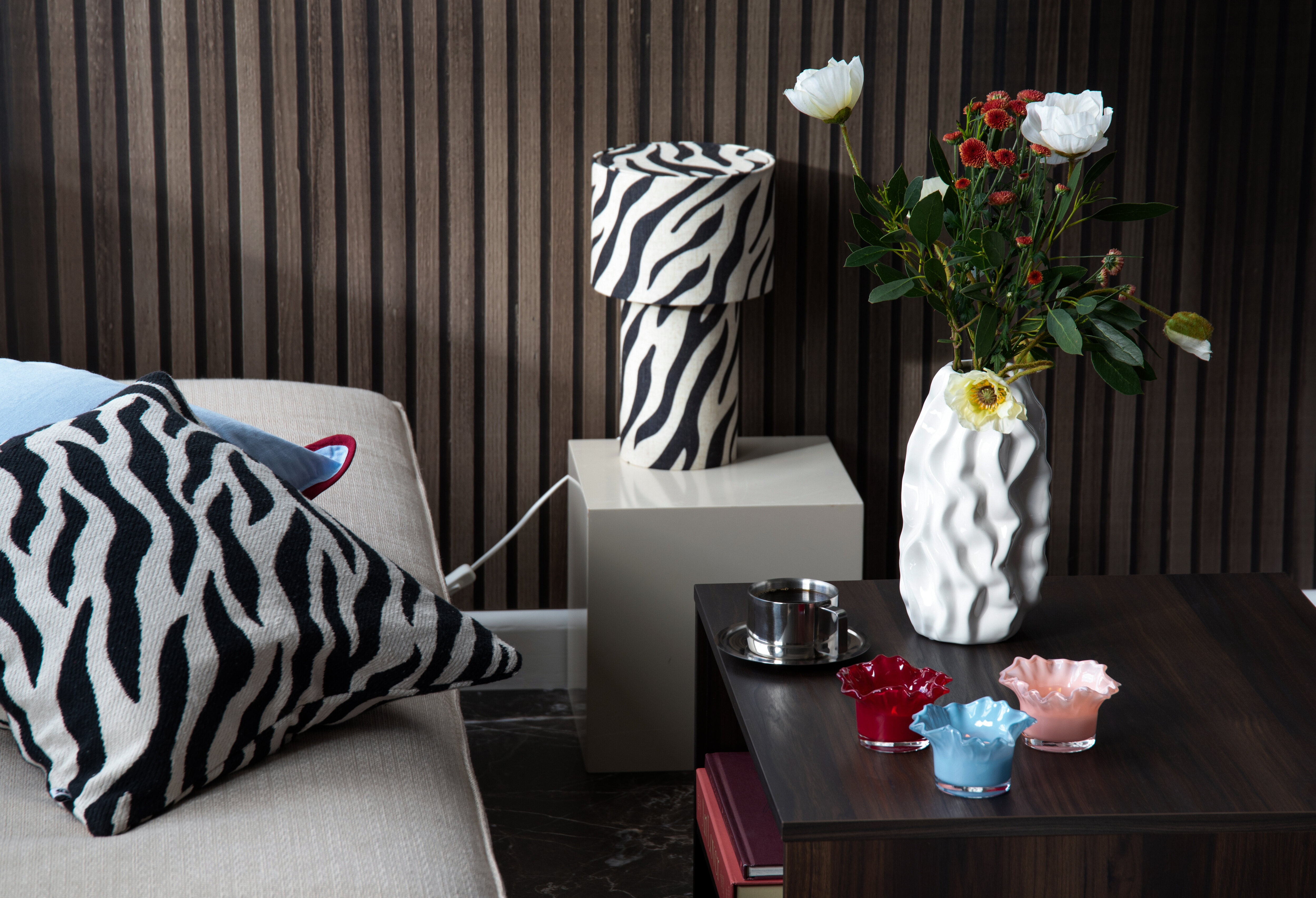 Zebra‑patterned lamp, cushion, and a vase with flowers on a table in a decorated room.