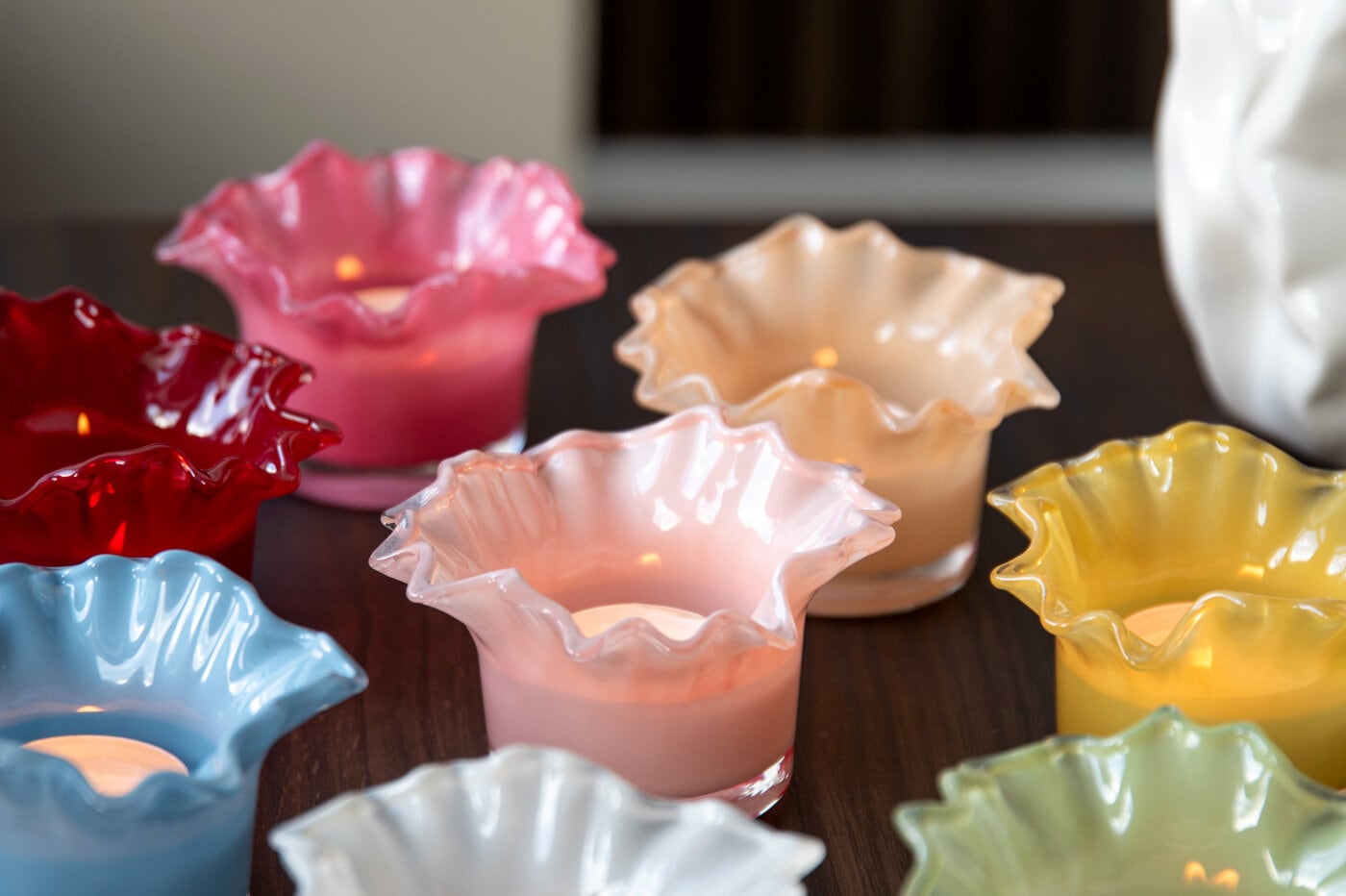 Colourful ruffled glass tealight holders with lit candles on a wooden table.