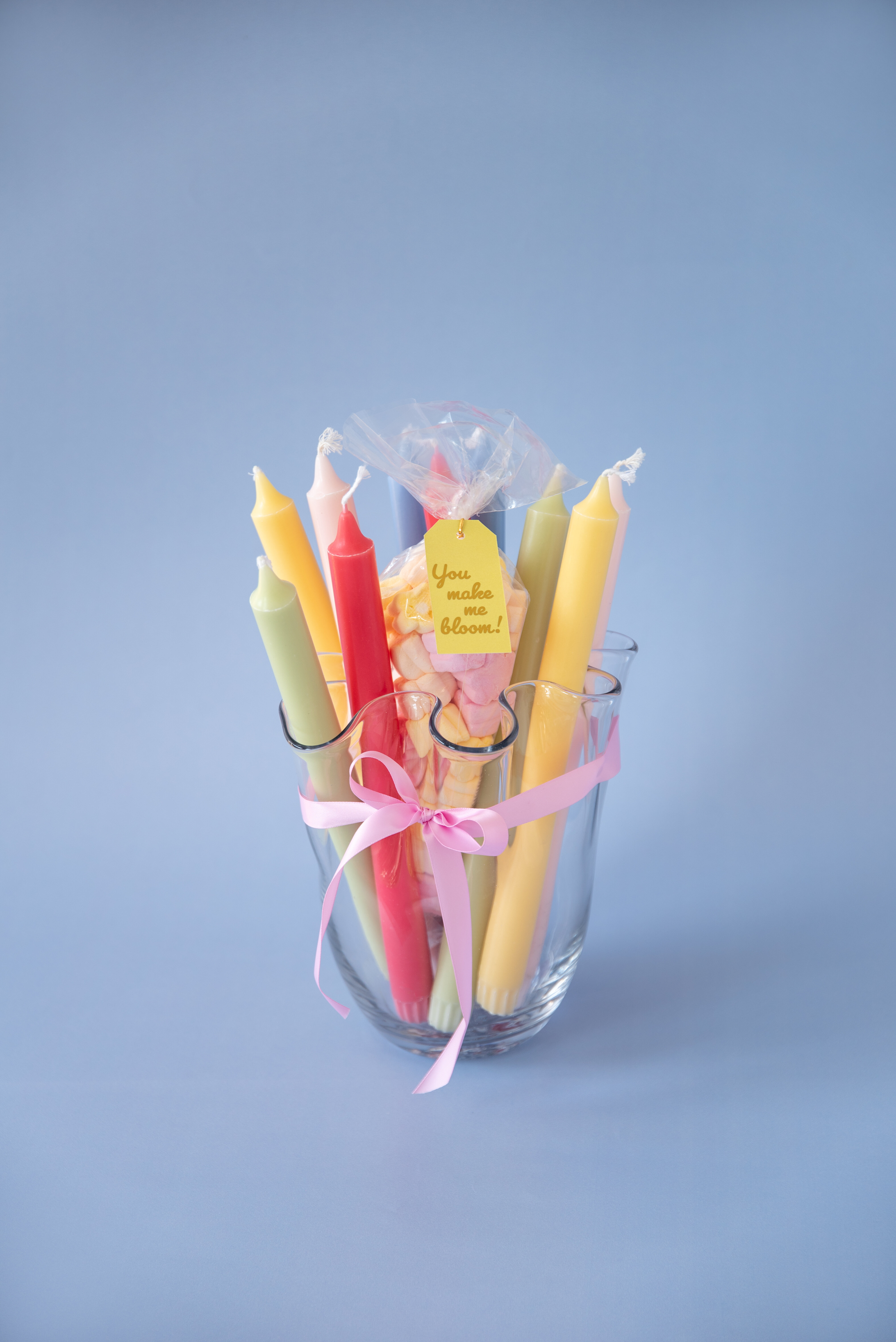 Colourful candles wrapped with ribbon in a glass vase.