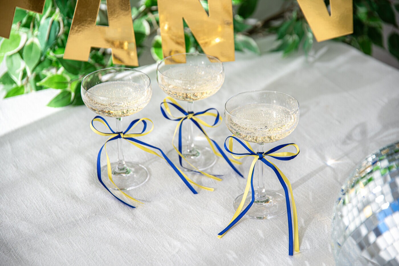 Champagneglas dekorerade med blågula band står på en vit duk.
