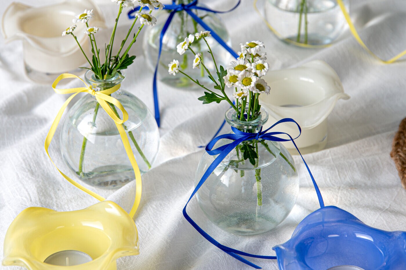 Glasvaser med små blommor dekorerade med blå och gula band på ett dukat bord.
