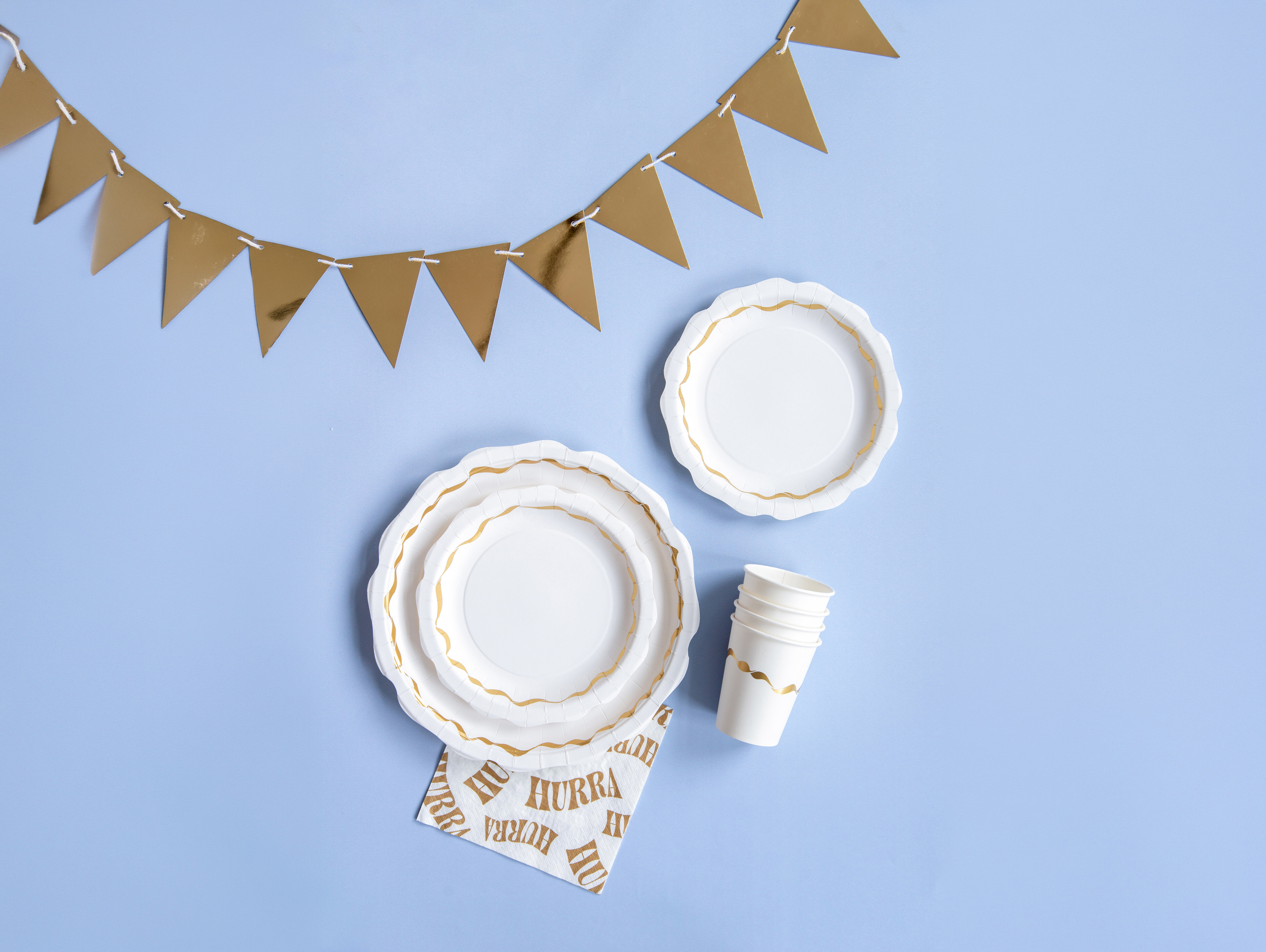 White disposable plates and cups with gold-coloured details and a gold-coloured bunting garland.