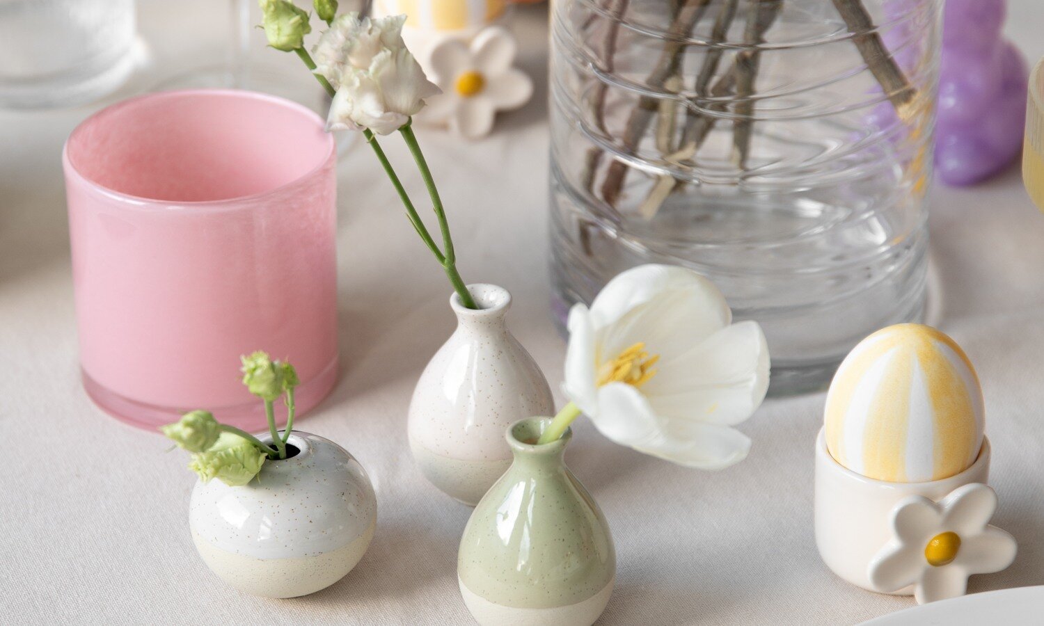 Small pastel-colored vases, white flowers, and a pink candle on a table