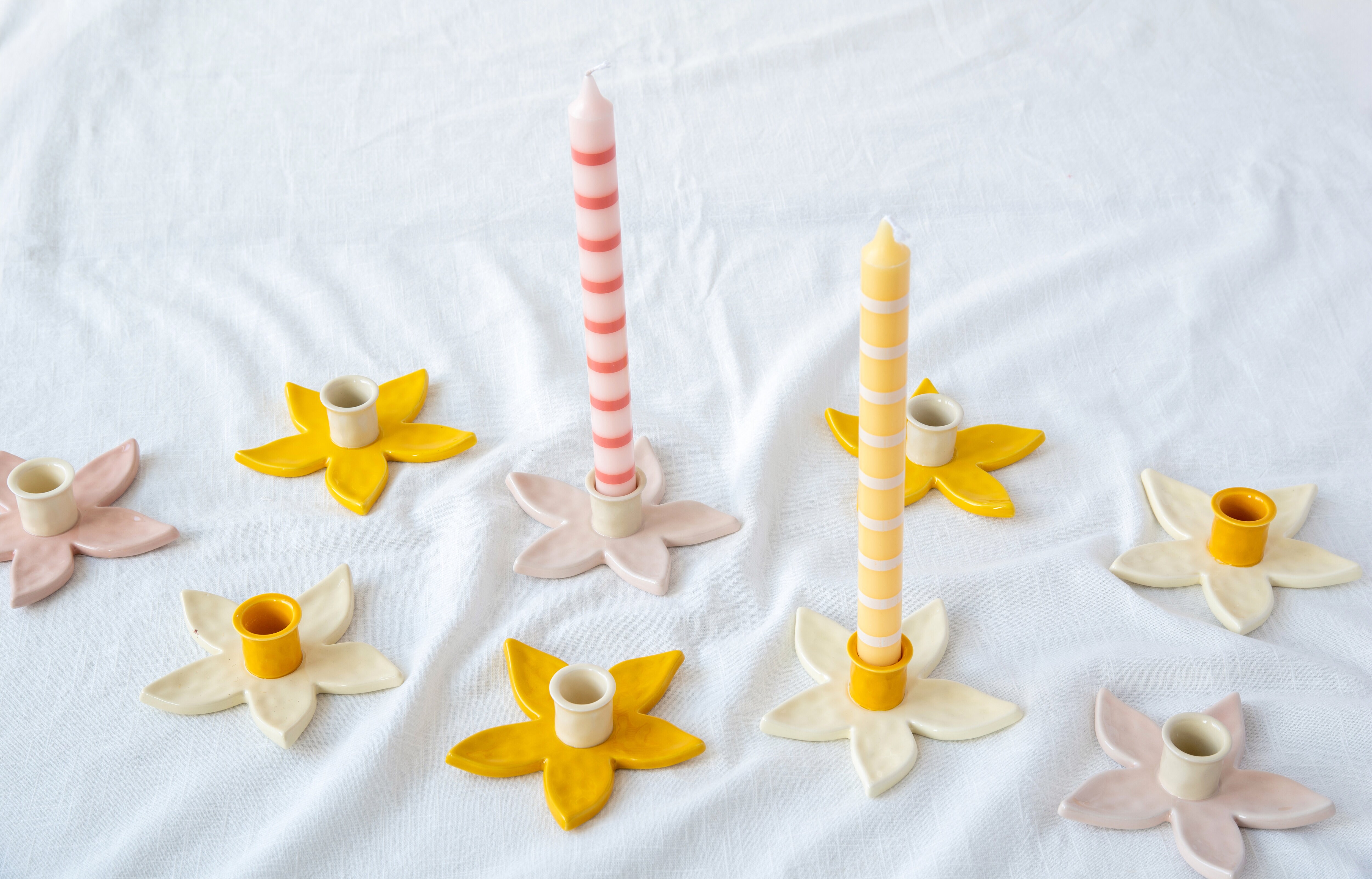 Flower-shaped candle holders with candles on a white tablecloth.