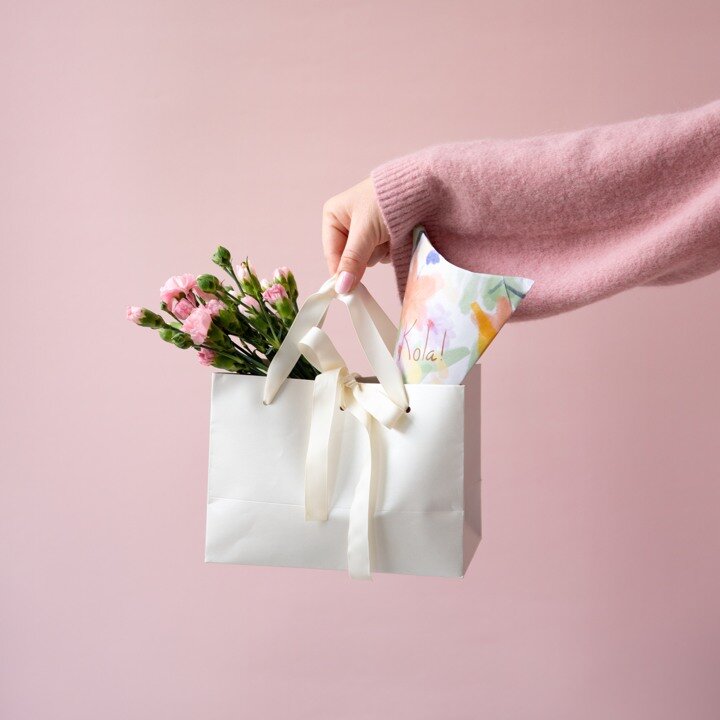 Hand holding a gift bag with flowers.