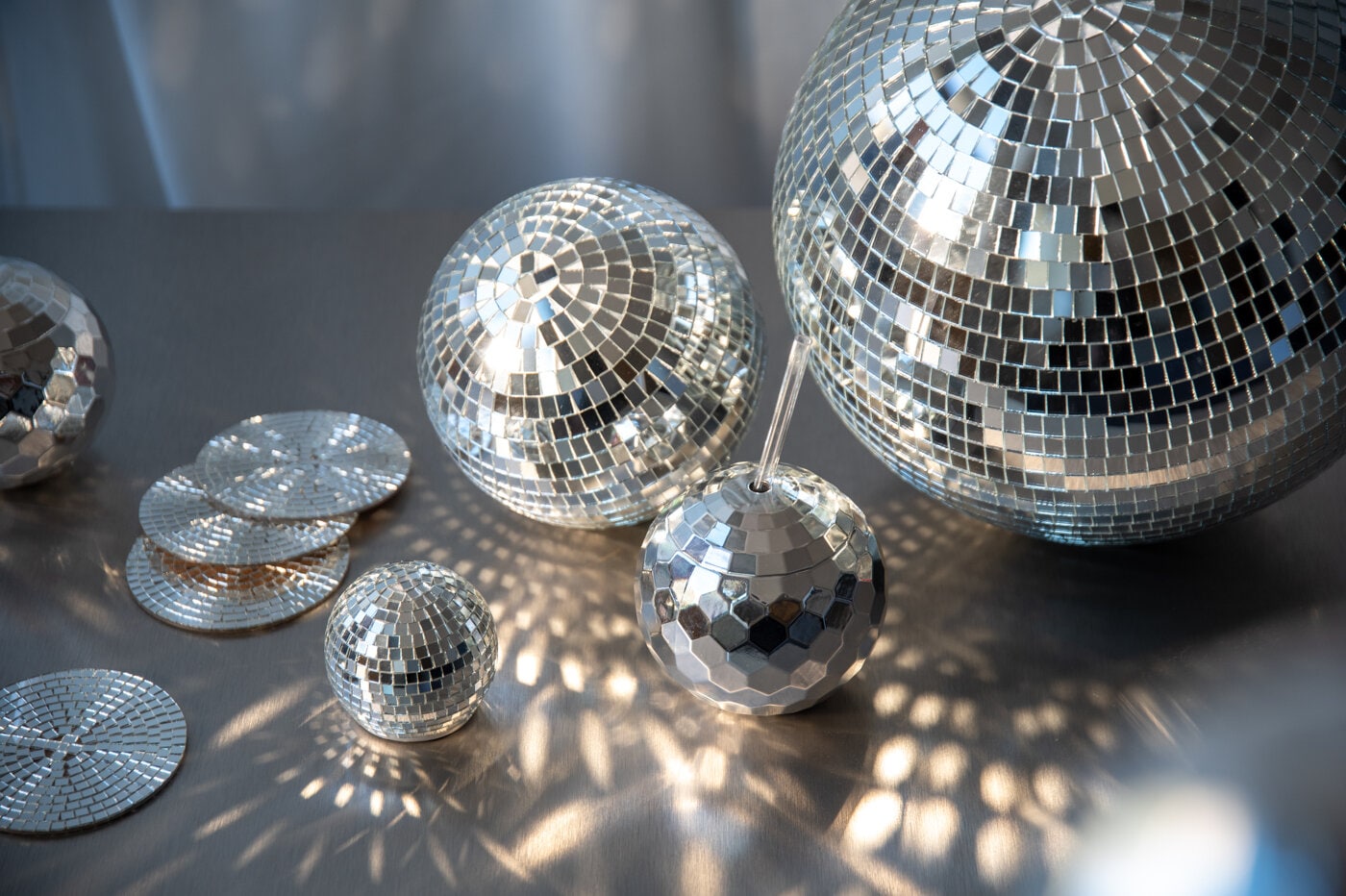 Silvriga discokulor, en silvrig mugg och silvriga glasunderlägg placerade på ett bord.