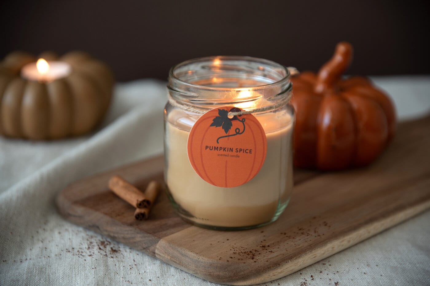 Scented candle in a glass jar with decorative pumpkin-tag.