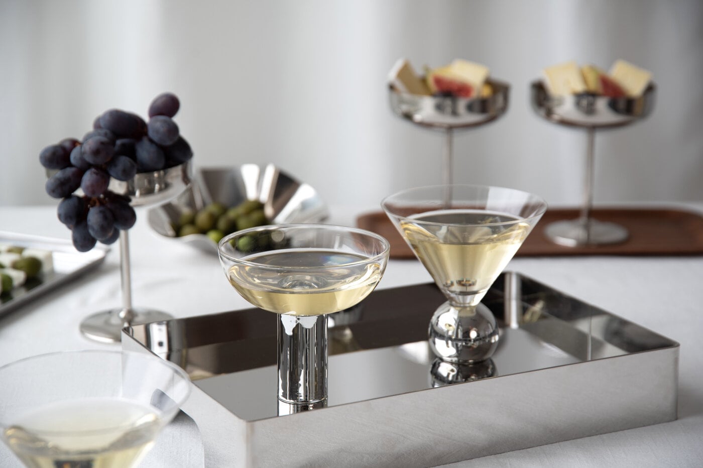 Cocktail glasses and serving stands with grapes and snacks on a table.