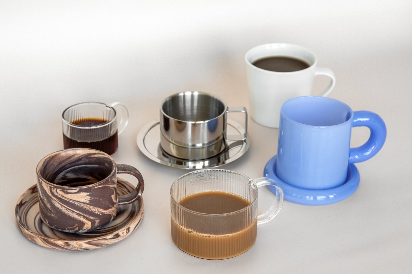 Mugs and cups in different colours and materials filled with coffee and hot drinks.