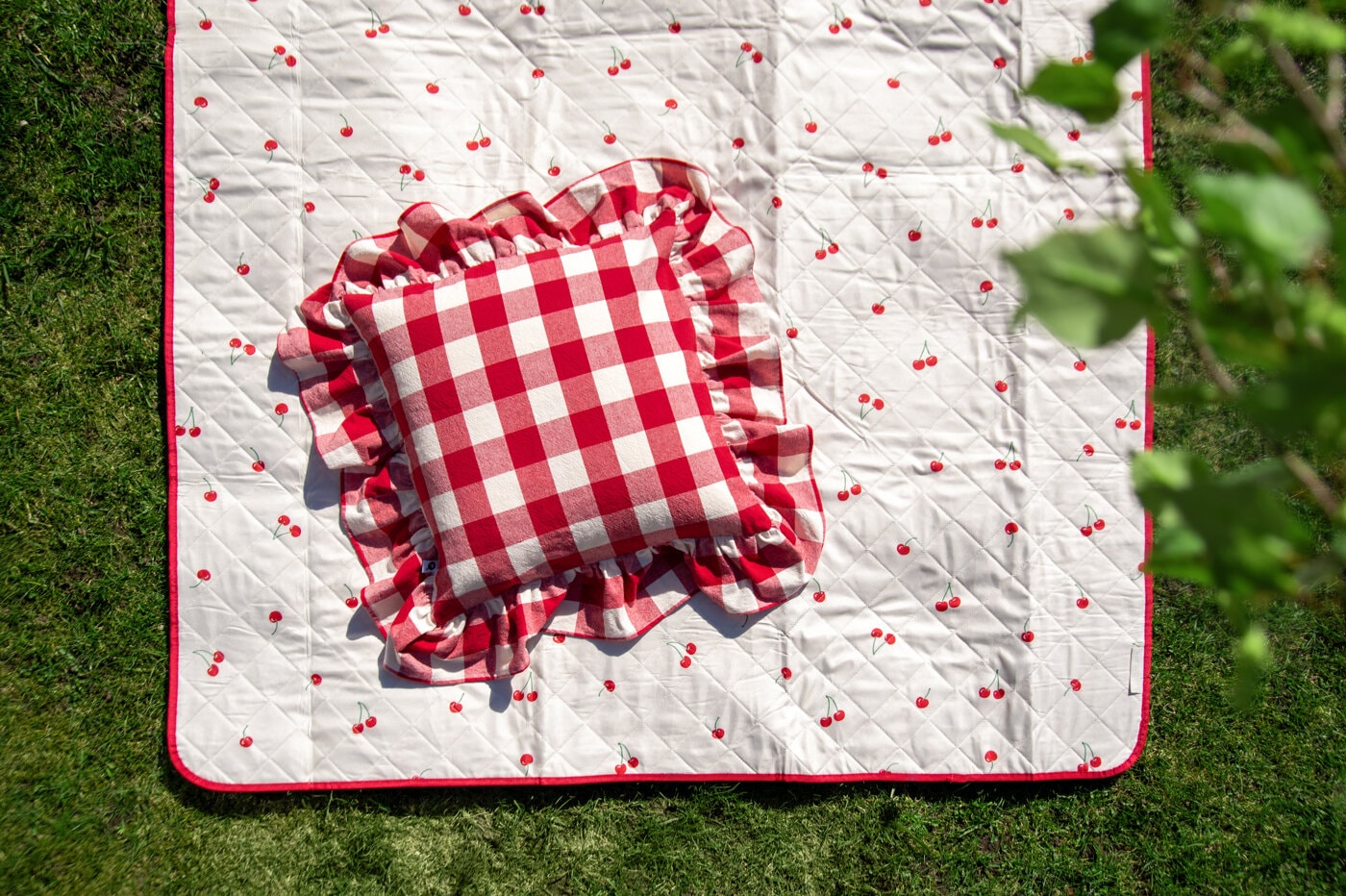 Picnic blanket with cherries and a red and white pillow.