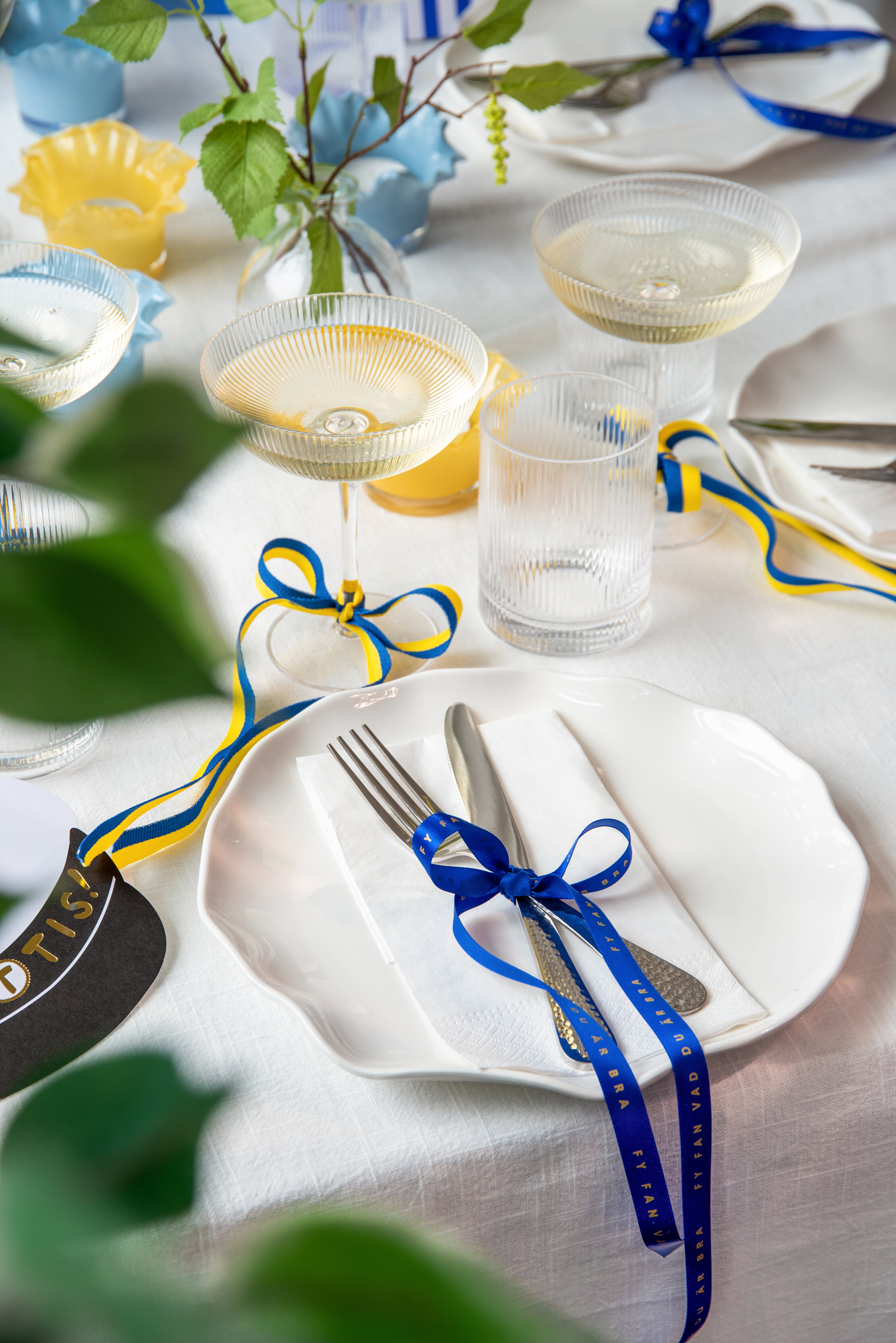 Dukat bord med glas, servetter och blå‑gula band.