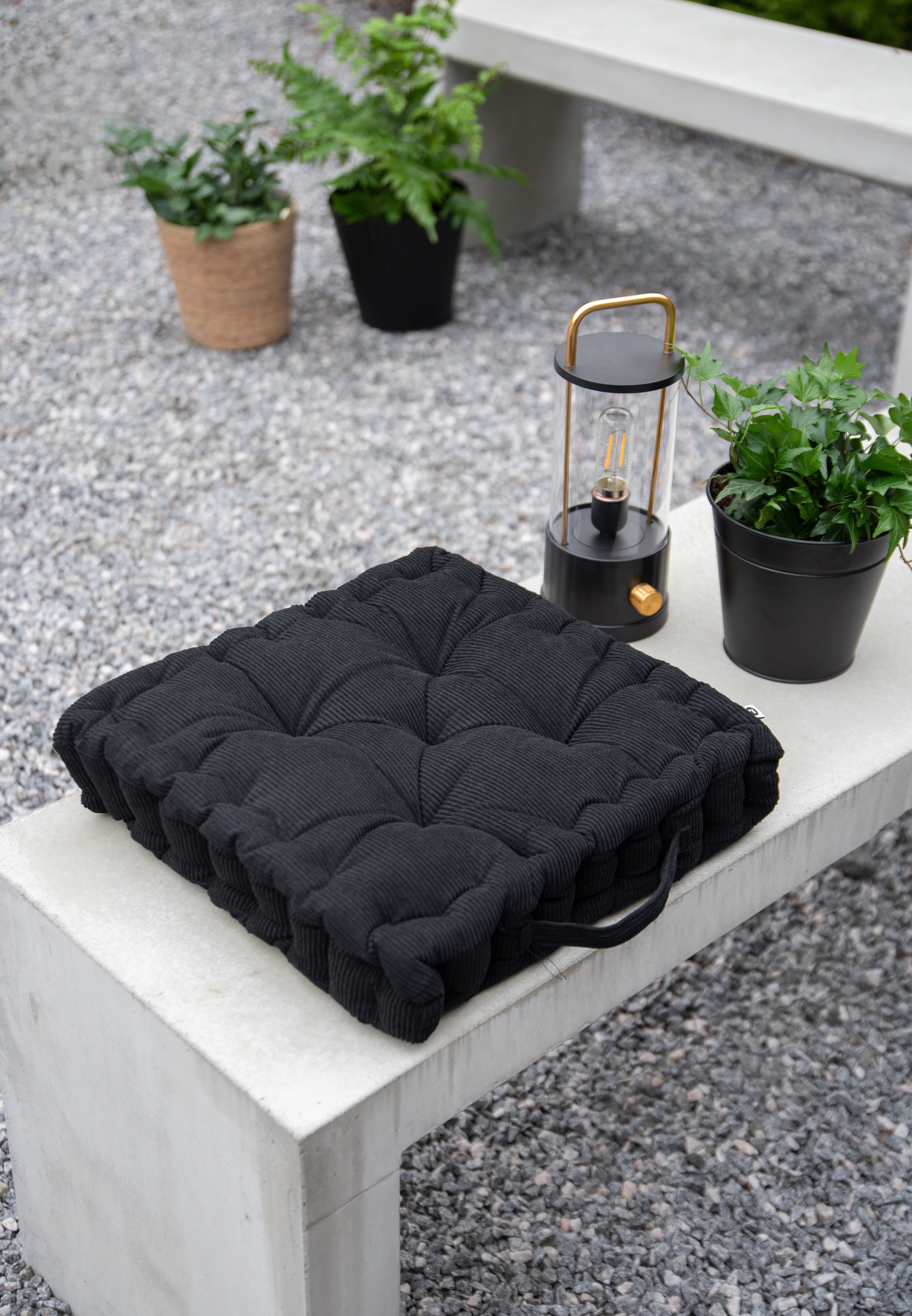 Black seat cushion on a patio with a lantern and potted plants.