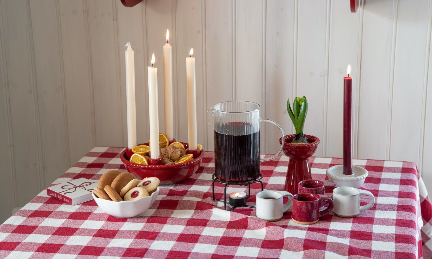 Juldukning med glögg, småkakor och ljus på rödvitrutig duk.