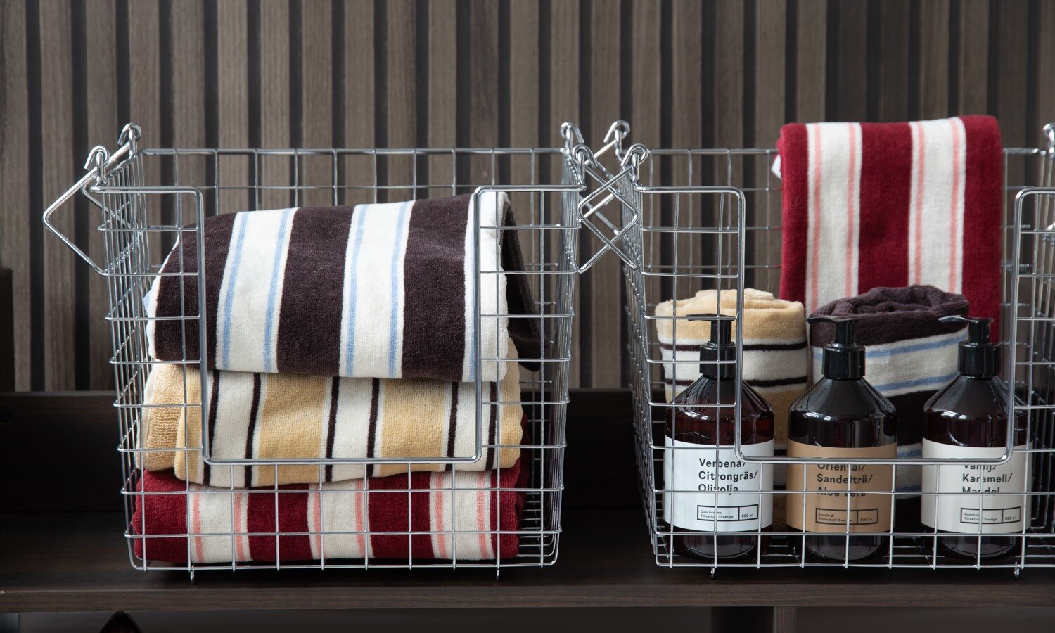 Wire storage baskets filled with striped towels and bottles of hand soap displayed in a bathroom setting.
